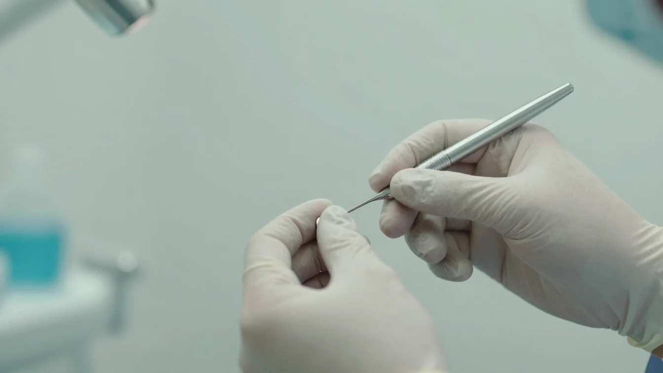 A close-up of a dentist's hands wearing gloves, gently cleaning teeth with a small tool, soft bright daylight, calm mute